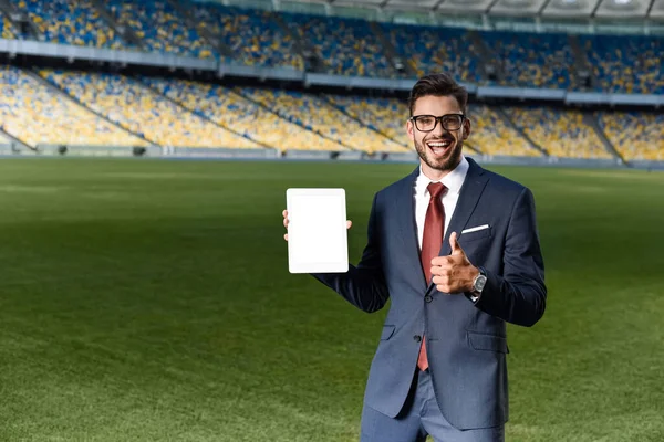 Jovem empresário feliz em terno e óculos segurando tablet digital com tela em branco e mostrando o polegar no estádio — Fotografia de Stock
