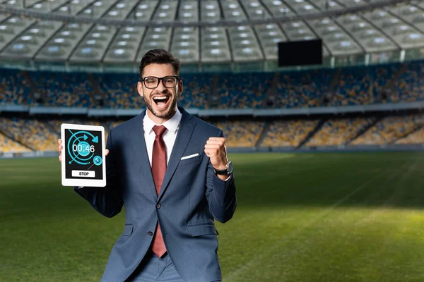Jovem empresário alegre em terno e óculos segurando tablet digital com aplicativo e mostrando sim gesto no estádio — Fotografia de Stock