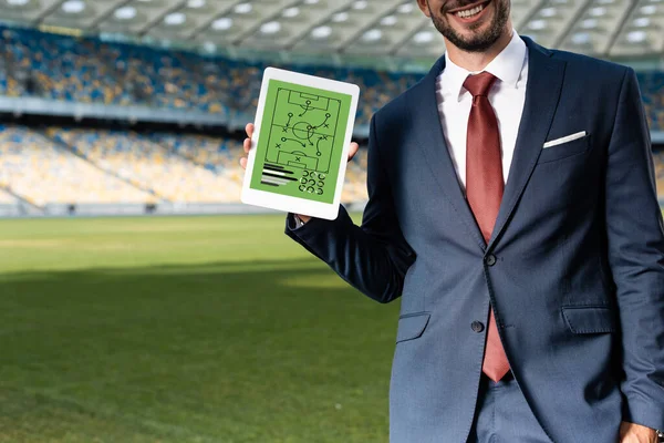 Cropped view of smiling young businessman in suit holding digital tablet with formation on screen at stadium — Stock Photo