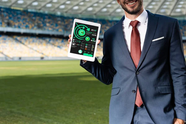 Cropped view of smiling young businessman in suit holding digital tablet with infographic app at stadium — Stock Photo