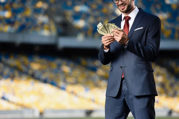 Vista recortada de joven hombre de negocios sonriente en traje y gafas con dinero en el estadio - foto de stock
