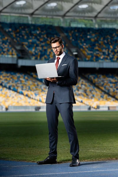 Young businessman in suit with laptop at stadium — Stock Photo