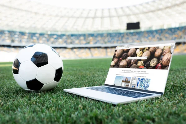 KYIV, UKRAINE - JUNE 20, 2019: soccer ball and laptop with depositphotos website on grassy football pitch at stadium — Stock Photo