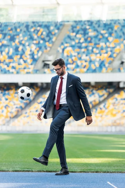 Giovane uomo d'affari in giacca e cravatta e occhiali che gioca con pallone da calcio allo stadio — Foto stock
