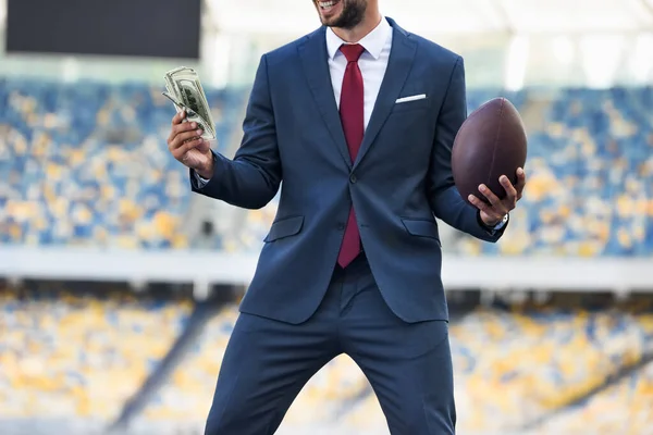 Ausgeschnittener Blick auf glücklichen jungen Geschäftsmann im Anzug mit Rugbyball und Geld im Stadion — Stockfoto