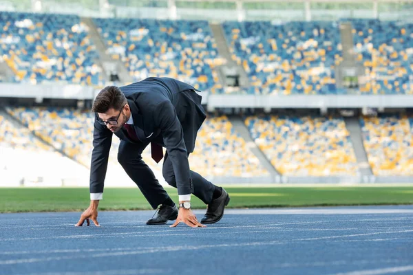 Young businessman in suit in start position on running track at stadium — Stock Photo