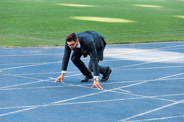 Young businessman in suit in start position on running track at stadium — Stock Photo