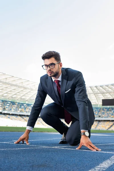 Joven hombre de negocios en traje en posición de inicio en pista de atletismo en el estadio - foto de stock