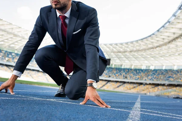 Vista recortada de joven hombre de negocios en traje en posición de inicio en pista de atletismo en el estadio - foto de stock