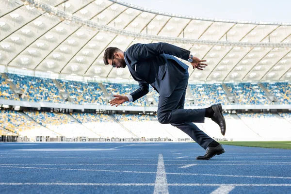 Vista lateral del joven hombre de negocios en traje corriendo en el estadio — Stock Photo