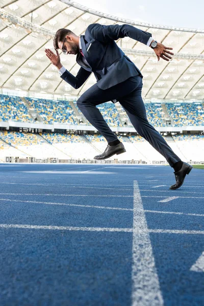 Vista lateral del joven hombre de negocios en traje corriendo en el estadio - foto de stock