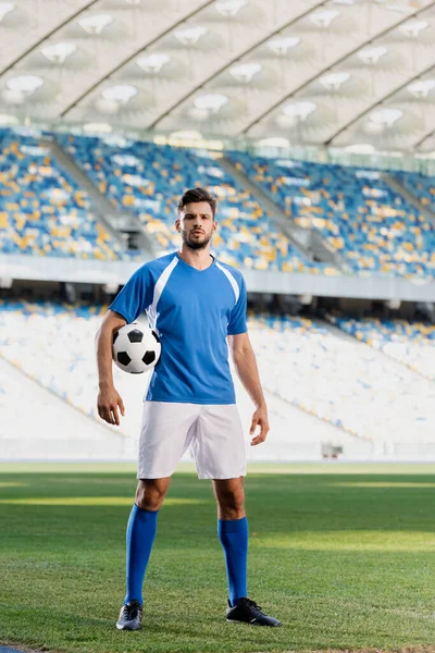 Calciatore professionista in divisa blu e bianca con palla sul campo da calcio dello stadio — Foto stock