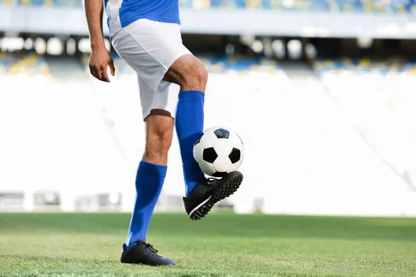 Cropped view of professional soccer player in blue and white uniform playing with ball on football pitch at stadium — Stock Photo