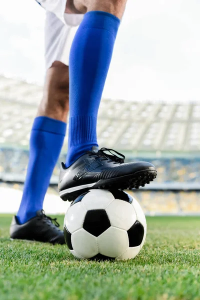 Legs of professional soccer player in blue socks and soccer shoes on ball at stadium — Stock Photo