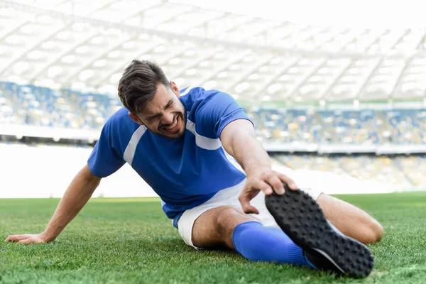 Jogador de futebol profissional em uniforme azul e branco que se estende no campo de futebol no estádio — Fotografia de Stock