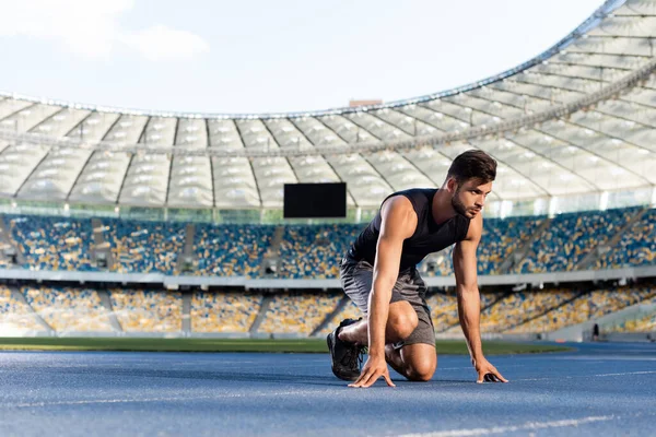 Handsome runner in start position on running track at stadium — Stock Photo