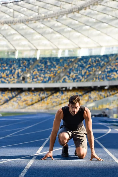 Apuesto corredor en posición de inicio en pista de atletismo en el estadio - foto de stock