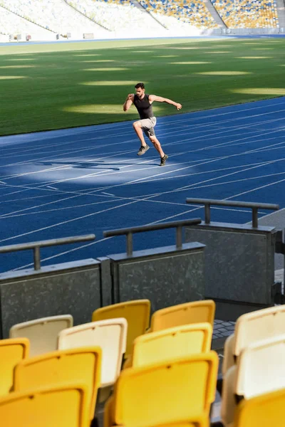 Selective focus of seats and fast handsome runner exercising on running track at stadium — Stock Photo