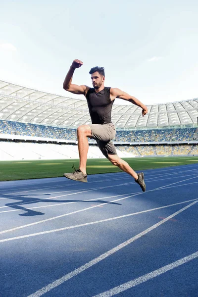 Apuesto corredor ejercitando en pista de atletismo en el estadio - foto de stock