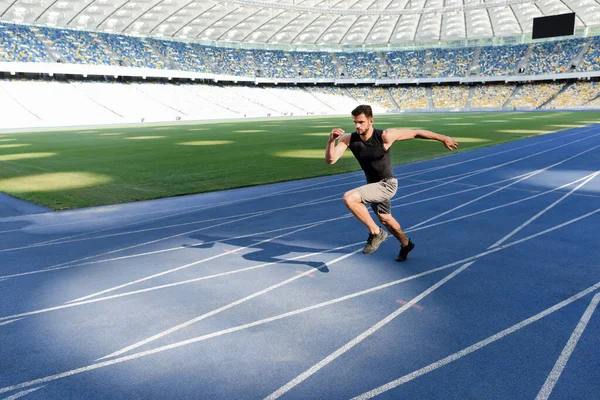 Apuesto corredor ejercitando en pista de atletismo en el estadio - foto de stock