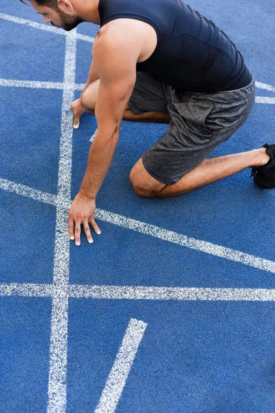 Vista recortada del corredor en posición de inicio en pista de atletismo en el estadio - foto de stock