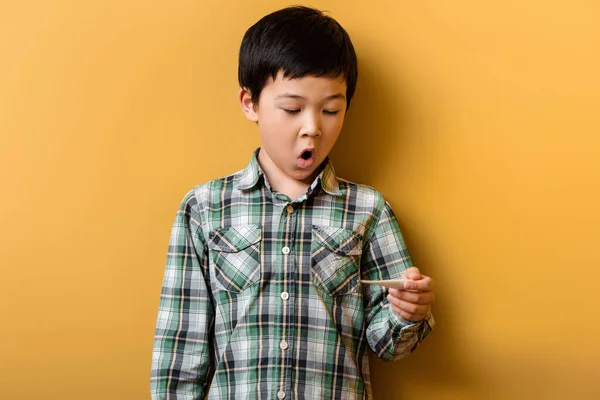 Shocked asian boy holding thermometer on yellow — Stock Photo