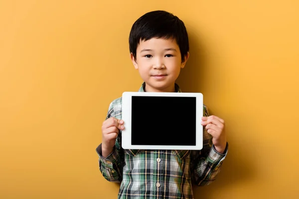 Ásia menino segurando digital tablet com branco tela no amarelo — Fotografia de Stock