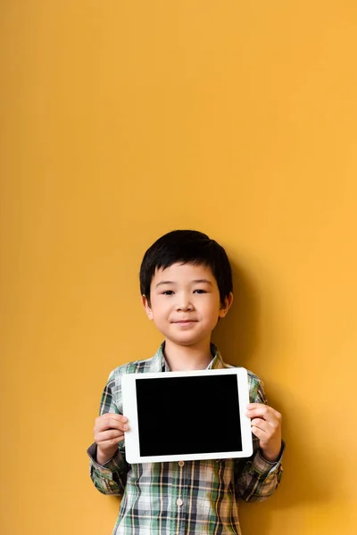 Bonito ásia menino segurando digital tablet com branco tela no amarelo — Fotografia de Stock