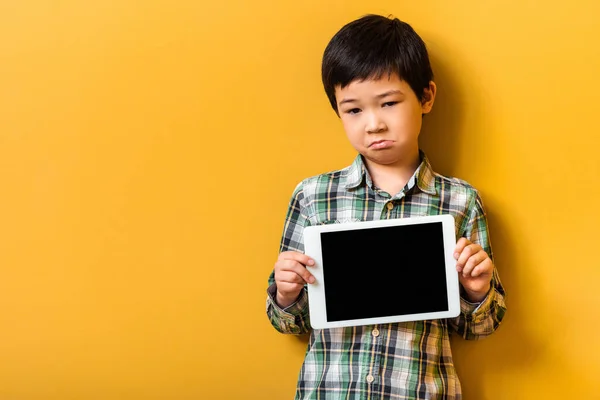 Chico asiático molesto con tableta digital con pantalla en blanco en amarillo. — Stock Photo