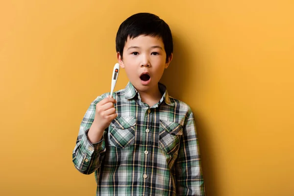 Sorpreso asiatico ragazzo holding termometro su giallo — Foto stock