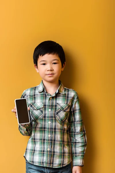 Азіатський хлопчик тримає смартфон з порожнім екраном на жовтому — стокове фото