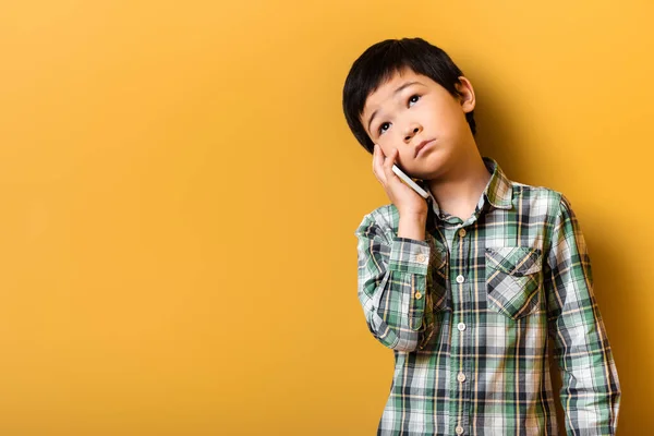 Chico asiático triste hablando por teléfono inteligente en amarillo - foto de stock