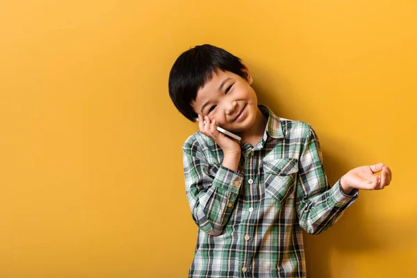 Felice asiatico ragazzo parlando su smartphone su giallo — Foto stock