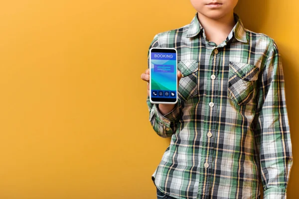 Sad asian garçon tenant un smartphone avec application de réservation en jaune — Photo de stock