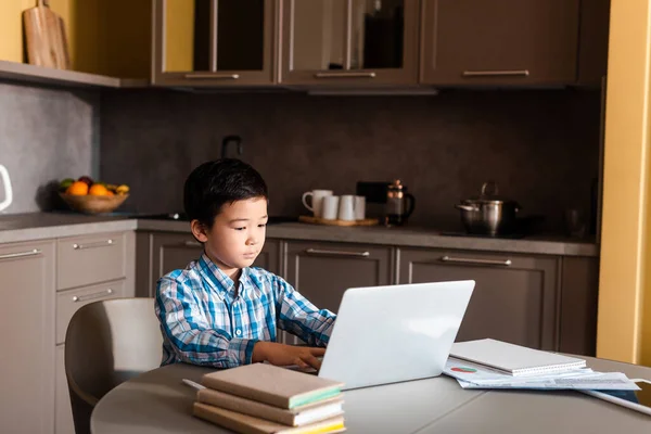 Chico asiático estudiando en línea con laptop y libros en casa durante el autoaislamiento. - foto de stock
