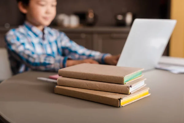 Chico asiático estudiando en línea con laptop y libros en casa durante la cuarentena, enfoque selectivo. - foto de stock