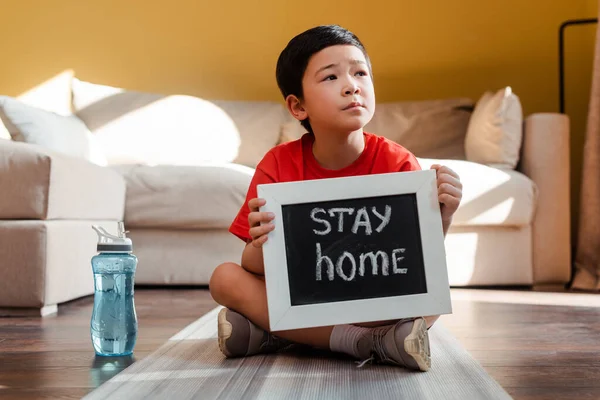 Suplemento de niño asiático con carta de estancia en casa sentado en el gimnasio con botella de deporte durante el autoaislamiento. - foto de stock