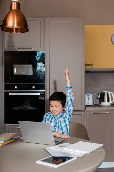 Mignon garçon asiatique avec main up étudiant en ligne avec ordinateur portable à la maison pendant l'auto isolement — Photo de stock