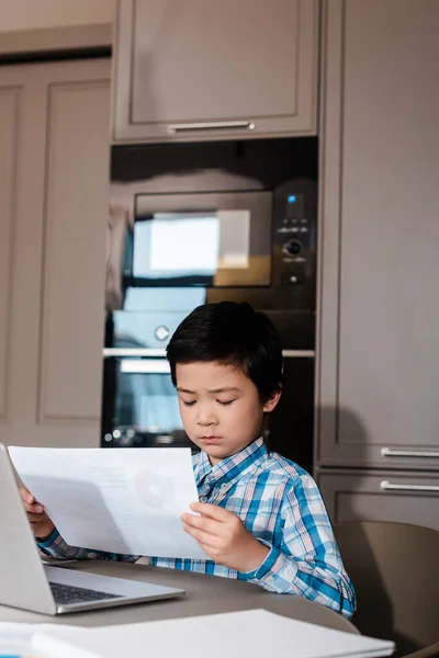 Asian boy studying online with papers and laptop at home during self isolation — Stock Photo