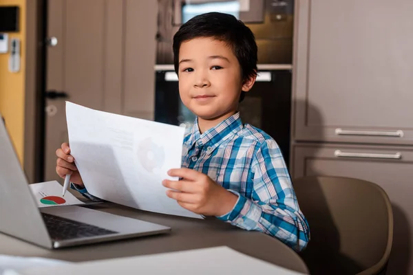 Happy asian boy studying online with papers and laptop at home during self isolation — Stock Photo