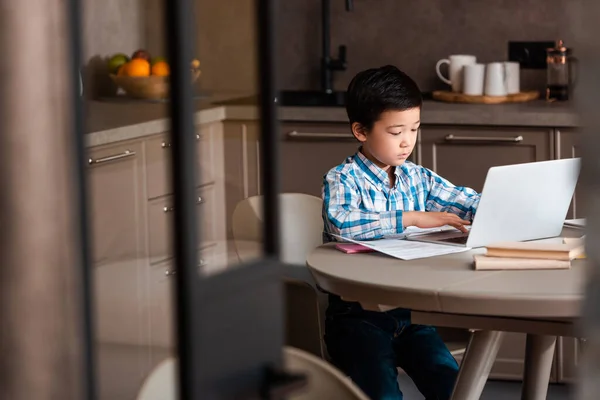 Chico asiático estudiando en línea con portátil en casa durante el autoaislamiento, enfoque selectivo. - foto de stock