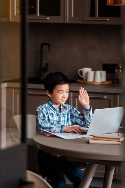 Asian boy with hand up studying online with laptop at home during self isolation, selective focus — Stock Photo