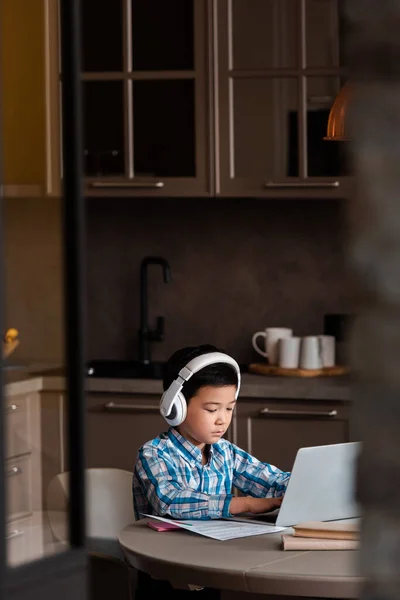 Asian boy studying online with books, laptop and headphones at home during quarantine — Stock Photo