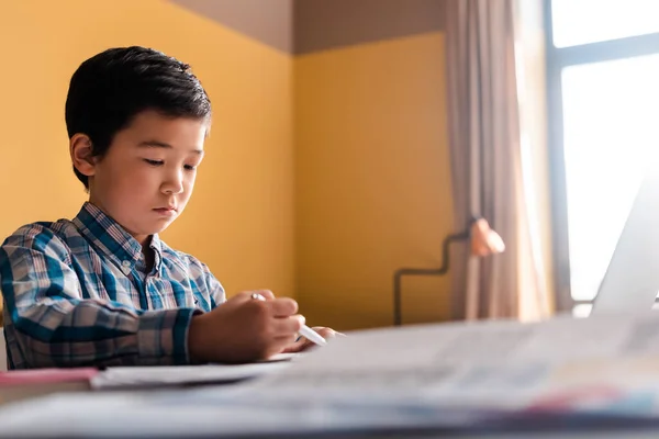 Азіатський хлопчик пише і вивчає онлайн з ноутбуком вдома під час карантину — стокове фото