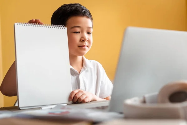 Chico asiático estudiando en línea con cuaderno y portátil en casa durante la cuarentena. - foto de stock