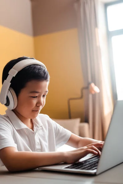 Chico asiático estudiando en línea con portátil y auriculares en casa durante la cuarentena. - foto de stock