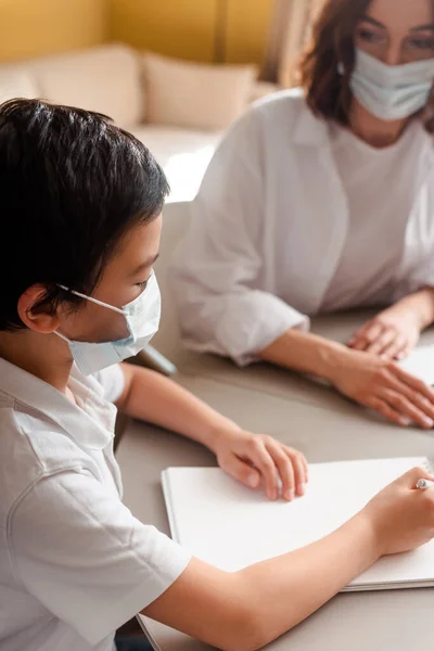 Asian boy in medical mask studying with mother at home on self isolation — Stock Photo