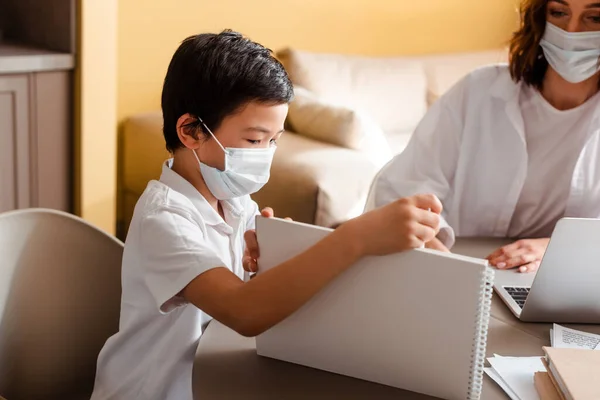 Asiatico ragazzo in medico maschera studiare con madre a casa su quarantena — Foto stock