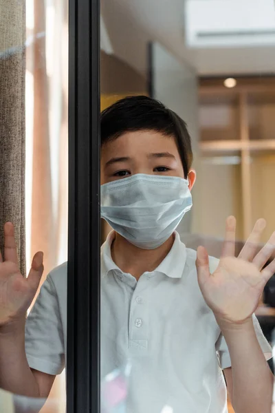 Bonito ásia menino no médico máscara olhando através de janela no quarentena — Fotografia de Stock