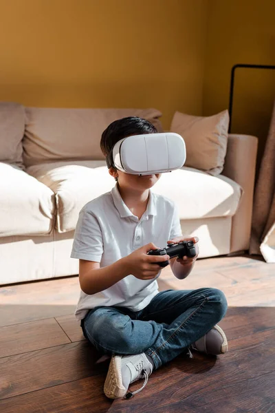 KYIV, UKRAINE - APRIL 22, 2020: los niños que juegan video juego con joystick y los auriculares de realidad virtual en el autoaislamiento. - foto de stock